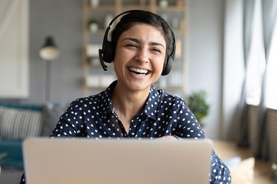 Das Bild zeigt eine Kursteilnehmerin mit Headset und lachend vor ihrem Laptop.